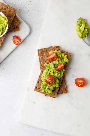 Top view of toast with avocado paste on bread with tomatoes cherry and arugula on white table. close...
