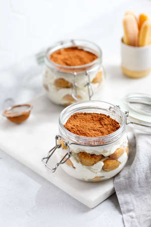 Pouring cocoa to tiramisu dessert. Traditional Italian dessert tiramisu in jars. Dessert made with savoiardi and cream decorated with cocoa powder.