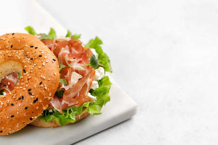 Sandwich with ricotta, prosciutto and microgreens, bagel with ham for breakfast on marble board....