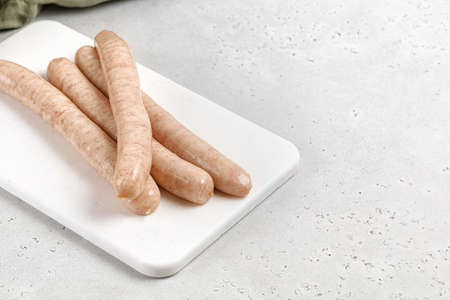 Raw barbecue sausages on white cutting board. Uncooked long Pork or Chicken sausages on gray background. Copy space, text place.の写真素材