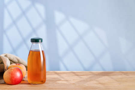 Homemade fresh Apple cider, vinegar, juice in glass bottle and fresh apples on wooden table. window shadow. copyspace.の写真素材