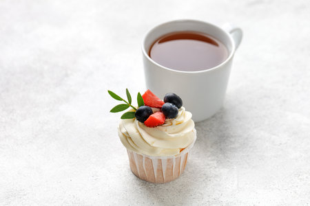 Cupcake with fresh berries, vanilla cream, green leaves with cup of tea on gray background. homemade dessert.の写真素材