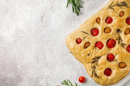 Italian focaccia bread with garlic, cherry tomatoes, rosemary and olive oil. Freshly homemade baked flat garlic bread. Top view, copy space.の写真素材
