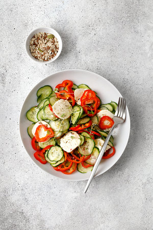 Sliced salad with Cucumbers, sweet peppers, feta cheese, micro greens on white plate with fork on gray background, top view. Copy space, place for text.の写真素材