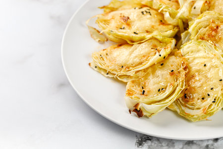 Baked cabbage pieces, roasted cabbage steaks with cheese on marble board and white background. Vegan diet, healthy food.の写真素材