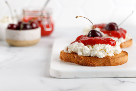 Toast, snack, bruschetta. Appetizer with ricotta cheese, cream cheese, jam and cherry on white board and marble table.の写真素材