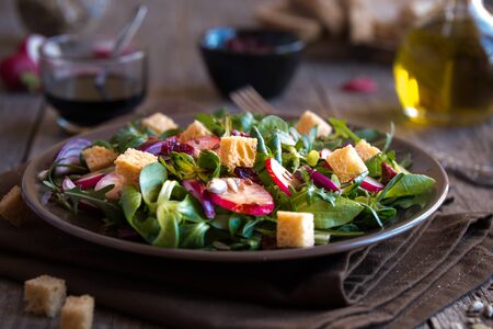 Fresh vegetable salad with radish, arugola, croutons on dark woodの写真素材