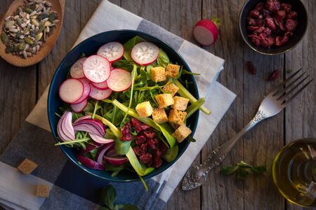 Fresh vegetable salad with radish, arugola, croutons on dark woodの写真素材