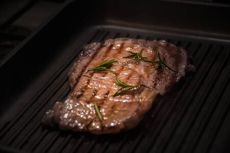 Raw beef meat, uncooked steak with rosemary, lemon and spices on black frying pan