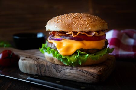 Hamburger with cheese, bacon, tomato and lettuce on dark wooden backgroundの写真素材