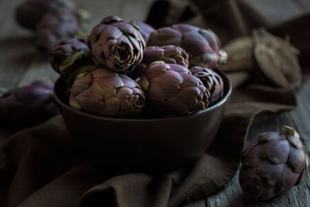 Fresh uncooked artichokes vegetables in a dark bowl, healthy food conceptの写真素材