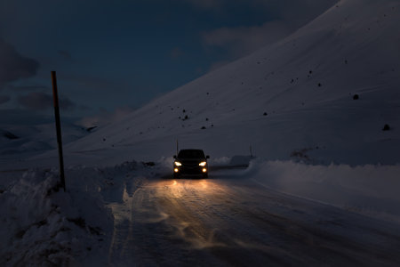 Car driving on winter road in dark surrounded by mountains covered with snowの写真素材