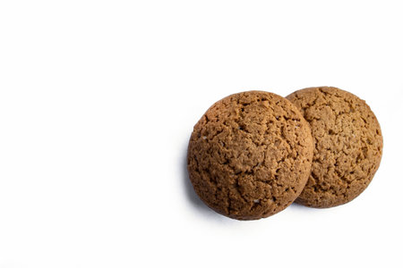 Two round oatmeal cookies resting on a clean white background, highlighting their golden texture and homemade charmの写真素材