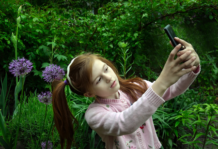 A girl is taking the selfy with a smartphone in a gardenの写真素材