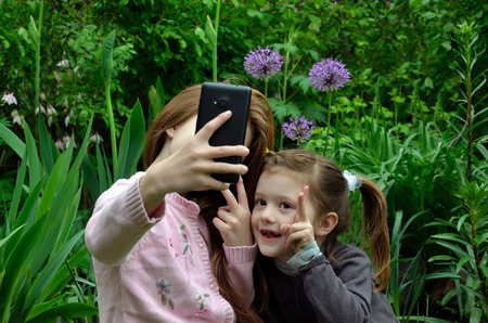 Two girls are taking the selfy with a smartphone in a gardenの写真素材