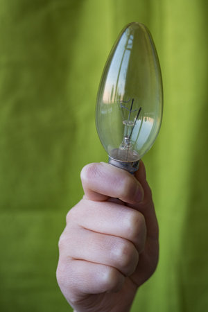 Hand holding a light bulb on a green background with space for textの写真素材