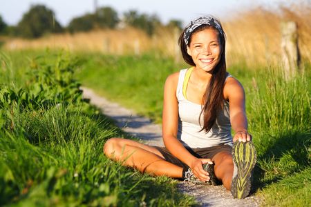 Woman stretching out during outdoor excercise a summer night. Sitting in the grass.の写真素材