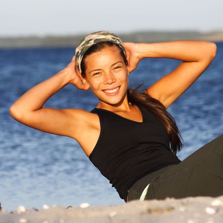 Woman doing situps / exercise outdoors on the beach with the ocean in the backgroundの写真素材