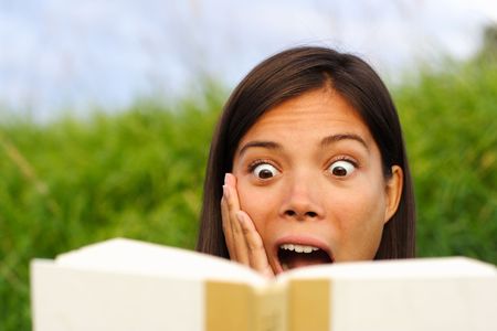 young beautiful woman surprised by the story she is reading in her book.