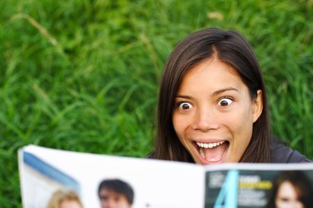 Excited woman surprised by gossip she is reading in magazine.の写真素材