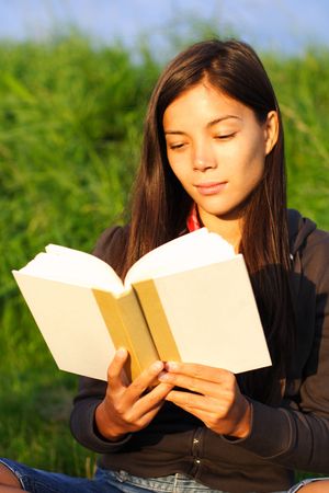Woman student reading book in warm evening light.の写真素材