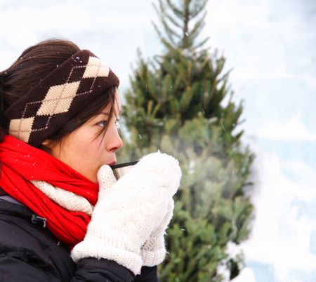 Woman drinking hot coffee or tea outdoors in winter. The background is an ice wall.