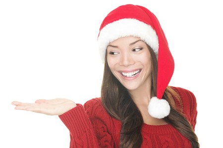 Closeup of Christmas woman showing your product in open hand palm. Happy Young smiling woman in Santa hat and red sweater looking to the side at copy space. Portrait Asian Caucasian woman isolated on white background. Excited version also available in porの写真素材