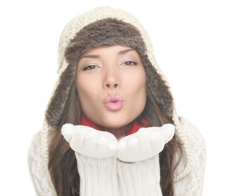 Winter woman isolated blowing kiss. Beautiful young lady in warm winter hat and clothing blowing a kiss to the camera.  Mixed Asian / Caucasian woman isolated on white background.の写真素材