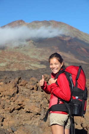 Healthy lifestyle concept- happy woman hiker giving thumbs up before the summit hike. Beautiful young Asian / Caucasian model. Image shows Pico Viejo from Teide National Park, Tenerife in the background with lots of copyspace.の写真素材
