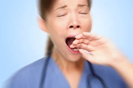 Tired young female nurse / doctor yawning at work. Young Asian / Caucasian woman model. Studio photo.の写真素材