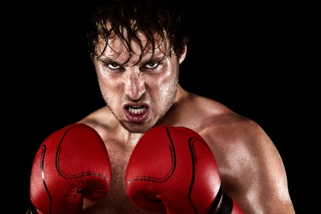 Boxer Boxing staring angry, mean and sweat showing strength. Young man looking aggressive with boxing gloves. Caucasian male model isolated on black background.の写真素材