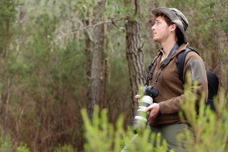 Photographer in nature taking pictures in forest. Outdoors man hiking with DSLR camera with tele...