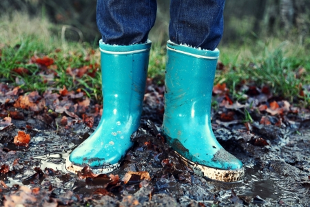 Fall / Autumn concept - Rain boots in mud puddle. Blue woman rain boots outdoors in action.