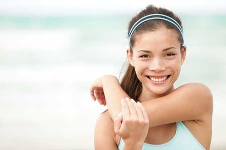 Fitness woman exercising smiling happy stretching out doing workout on beach. Beautiful mixed race Asian Caucasian female fitness model portrait.の写真素材