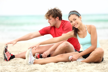Couple training on beach stretching legs after running. Young man and woman during summer workout....