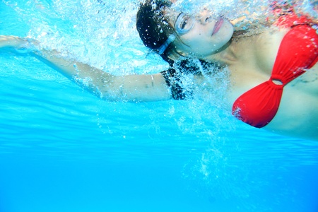 Swimming woman. Swimmer underwater image of girl swimming crawl in red bikini wearing swimming goggles.の写真素材