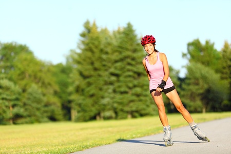 Skating woman on rollerblades in park. Girl going rollerblading sitting in grass putting on inline...