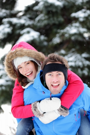 Young excited happy winter couple doing piggyback having fun outside in winter snow forest landscape  Happy young interracial couple, Caucasian man, Asian woman の写真素材