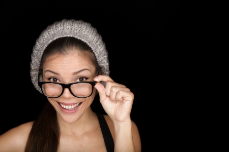 Cool hipster student woman wearing eyewear glasses and knit hat isolated on black background in studio. Beautiful multiracial mixed race Asian Chinese / Caucasian female university student looking at camera smiling happy.の写真素材