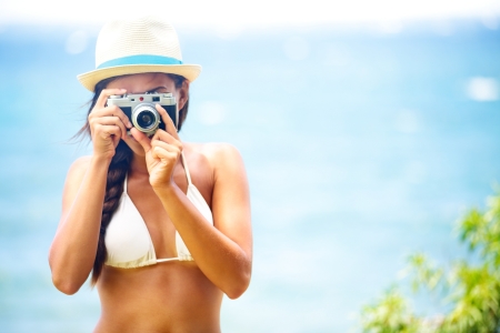 Summer beach woman holding vintage retro camera taking pictures looking at camera during summer holiday vacation travel at the ocean の写真素材