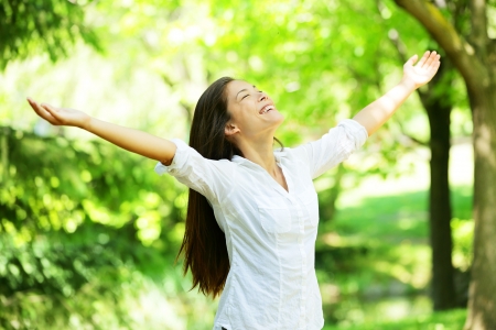 Young woman meditating with open arms standing in fresh spring greenery with her head raised to the sky and her eyes closed rejoicing in the freshness and new beginnings of spring and natureの写真素材