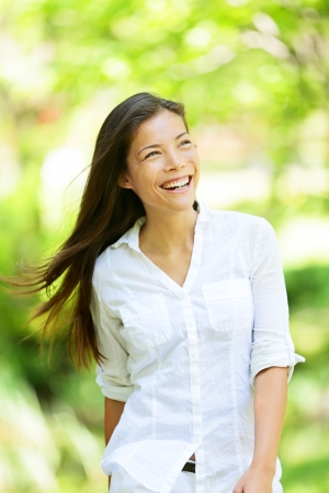 Joyful vivacious woman in a spring or summer park beaming a broad smile as she walks along rejoicing in the freshness of nature and the warm glow of the sunlight through the leaves of the green treesの写真素材