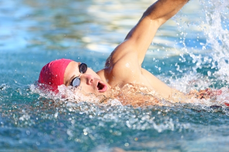 Man swimmer swimming crawl in blue water. Portrait of an athletic young male triathlete swimming crawl wearing a pink cap and swimming goggles while. Triathlete training for triathlon.の写真素材