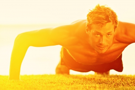 Sport fitness man push-ups. Male athlete exercising push up outside in sunny sunshine. Fit shirtless male fitness model in crossfit exercise outdoors. Healthy lifestyle concept.の写真素材