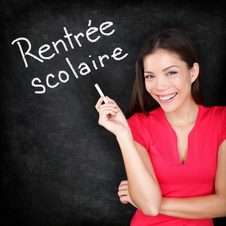 Rentree Scolaire - French teacher Back to School written in French on blackboard by woman teacher holding chalk. Smiling happy woman teaching French language or university student back in college.の写真素材