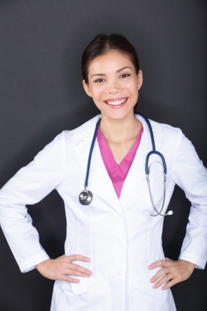 Female medical doctor woman portrait. Happy smiling young medical professional in lab coat with stethoscope looking at camera on black background. Multi-ethnic Asian Caucasian female model.の写真素材