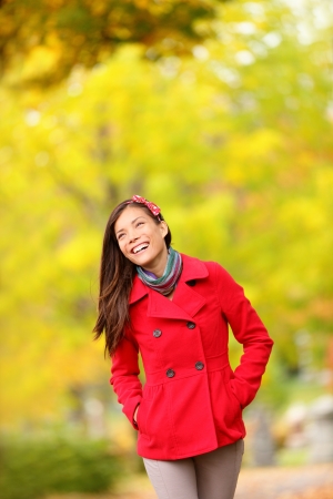 Fall woman walking amongst autumn trees. Beautfiul laughing young woman in a trendy red jacket walking amongst colourful yellow autumn trees with copy space. Mixed race Chinese Asian / Caucasian girl.の写真素材