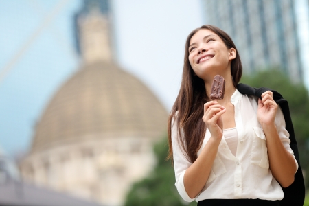 Business woman eating ice cream in Hong Kong. Young businesswoman enjoying ice-cream on at stick walking outside smiling happy in central Hong Kong. Mixed race Chinese Asian / Caucasian model on breakの写真素材
