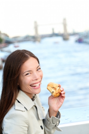 Scones - woman eating scone in London. Happy girl holding British pastry by River Thames, London, England, United Kingdomの写真素材