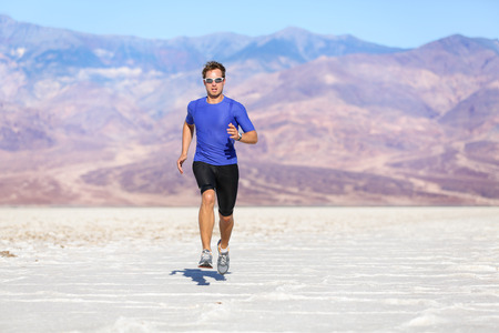 Running man - sprinting athlete runner in desert. Fit athletic male fitness model in fast sprint run at great speed towards camera. Sport in amazing extreme desert landscape.の写真素材